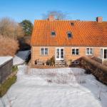 A house with red tiled roof and white entrance. The garden is covered in snow.
