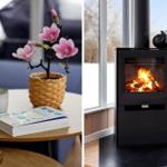 Table with flower, mug, and book. Fireplace with burning wood and window.