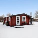 Red wooden house with white window frames covered in snow.