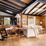 Living area with fireplace, dining table, and kitchen under wooden ceiling.