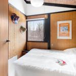 Bedroom with wooden walls, window, and bed with white bedding.