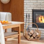 A fireplace with burning fire, wood in a basket, and a sofa with cushions.