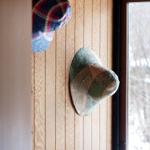 Two hats hang on a wooden wall next to a window with a view of snow.