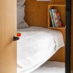 A bed with white bedding, pillows, and a bookshelf on the wall.