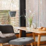 Table with teapot, bread, and flowers by window overlooking garden.