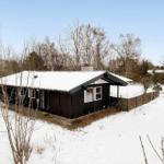 Black wooden house with snow-covered roof and garden fence.