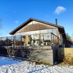 Modern wooden cabin with glass railing and snow in the front yard.