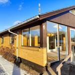 Modern vacation home with wooden facade and large glass windows. Wooden terrace with railing. Snow on ground.