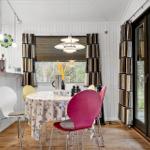 Essbereich mit runden Tisch und bunten Stühlen. Fenster und Glastür mit Vorhängen.