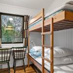 Zimmer mit Schlafcouch, Tisch und zwei Stühlen. Fenster mit Vorhängen. Holzboden.