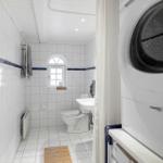 Badezimmer mit Toilette, Waschbecken und Fenster. Weiße Fliesen und Waschmaschine.