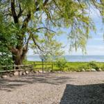 Gravelweg führt zu einem Haus mit Blick aufs Meer unter einem großen Baum.