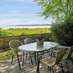 Terrasse mit Tisch und Stühlen, Blick auf Wasser und Grünflächen.