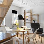 Essbereich mit runden Tisch, weißen Stühlen und Holzregalen an der Wand.