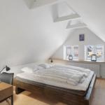 Schlafzimmer mit Dachschrägen, Bett, Schreibtisch und Fenster.