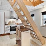 Küche mit Holztreppe zur oberen Etage. Fenster mit Pflanze und Heizkörper.