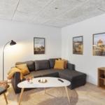 Ein Wohnzimmer mit grauem Sofa, weißem Tisch und Holzboden.