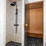 Shower with showerhead and sauna with wooden wall and bench.