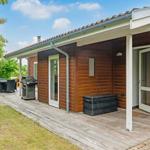 Wooden house with terrace, grill, and garden furniture under blue sky.
