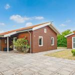 Wooden house with terrace, grill, and small outbuilding on paved grounds.