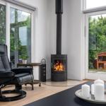 Black chair next to fireplace and windows with view of garden.