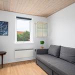 Living room with gray sofa, wooden floor, and wooden ceiling. Window with view of greenery.