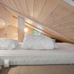 Double bed under sloped roof with wooden walls and window