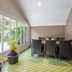 Terrace with table, six chairs, and plants. Large window front with view of greenery.