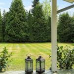 From the porch, you see a green lawn and tall evergreen trees.