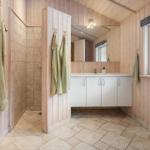 Bathroom with shower, sink, and window. Wooden walls and tiled floor.