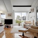 Wohnraum mit Sofa, Fernseher und Sessel. Holzboden und große Fenster.