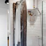 Dusche mit Glaswand, Duschvorhang und Regal. Weiße Fliesen und Heizung.