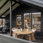 Terrasse mit Tisch, Stühlen und Grill. Blick ins Innere mit Küche und Wohnbereich.
