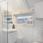 Badezimmer mit Dusche, Waschbecken und Toilette. Weiße Wände und Fenster mit Blick.