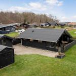 Schwarze Holzhütte mit Terrasse und Garten. Umgebung mit weiteren Häusern und Wald.