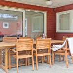 Terrasse mit Holztisch und Stühlen, rote Fassade, Fenster und Glastür.