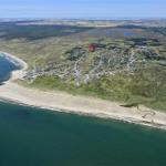 Luftbild eines Küstenorts mit Strand und grünen Hügeln. Ein roter Punkt markiert die Lage.