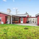 Rotes Ferienhaus mit Terrasse, Grill und Garten. Glasfront öffnet sich zum Innenraum.