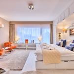 Schlafzimmer mit Bett, zwei orangefarbenen Sesseln und großem Fenster.