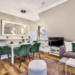 Essbereich mit grünen Stühlen und Wohnzimmer mit Sofa und Fernseher.