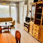 Wohnzimmer mit Sofa, Esstisch und Holzschrank. Große Fenster mit Blick.