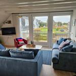 Wohnzimmer mit Sofa, Sessel und Balkonansicht.