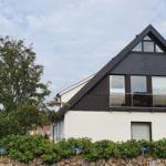 Modernes Haus mit Balkon und weißen Wänden. Umgeben von Grün und Steinmauer.