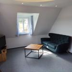 Wohnzimmer mit Sofa, Tisch und Fenster. Wandfarbe hell, Boden belegt.
