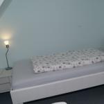 Schlafzimmer mit Bett, Nachttisch und Lampe unter Dachschrägen.