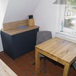 Küche mit Holztisch, Stühlen und dunklem Schrank. Fenster mit Blick nach draußen.