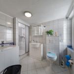 Badezimmer mit Dusche, Waschbecken und Toilette. Weiße Fliesen und Heizung.