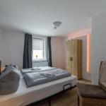 Schlafzimmer mit Doppelbett, Holzschrank und Fenster mit Vorhängen.