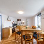 Küche mit Esstisch, Holzmöbel und Fenster. Tisch mit Obst und Wasser.