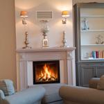 Ein Kamin mit brennendem Feuer, zwei Sessel und ein Schrank mit Ankerdekoration.